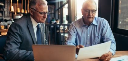Two men looking at a document and a file in a laptop.